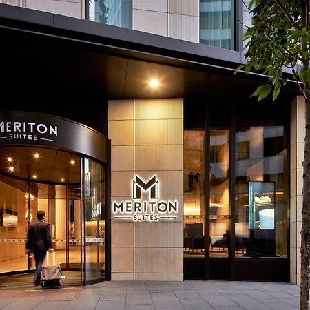 Meriton Suites Sussex Street, Sydney Zewnętrze zdjęcie The photo shows the entrance of a hotel or suite establishment named "Meriton Suites." The entrance features a revolving door and a large, illuminated sign with the name "MERITON SUITES." The facade is modern and sleek, with a combination of glass an