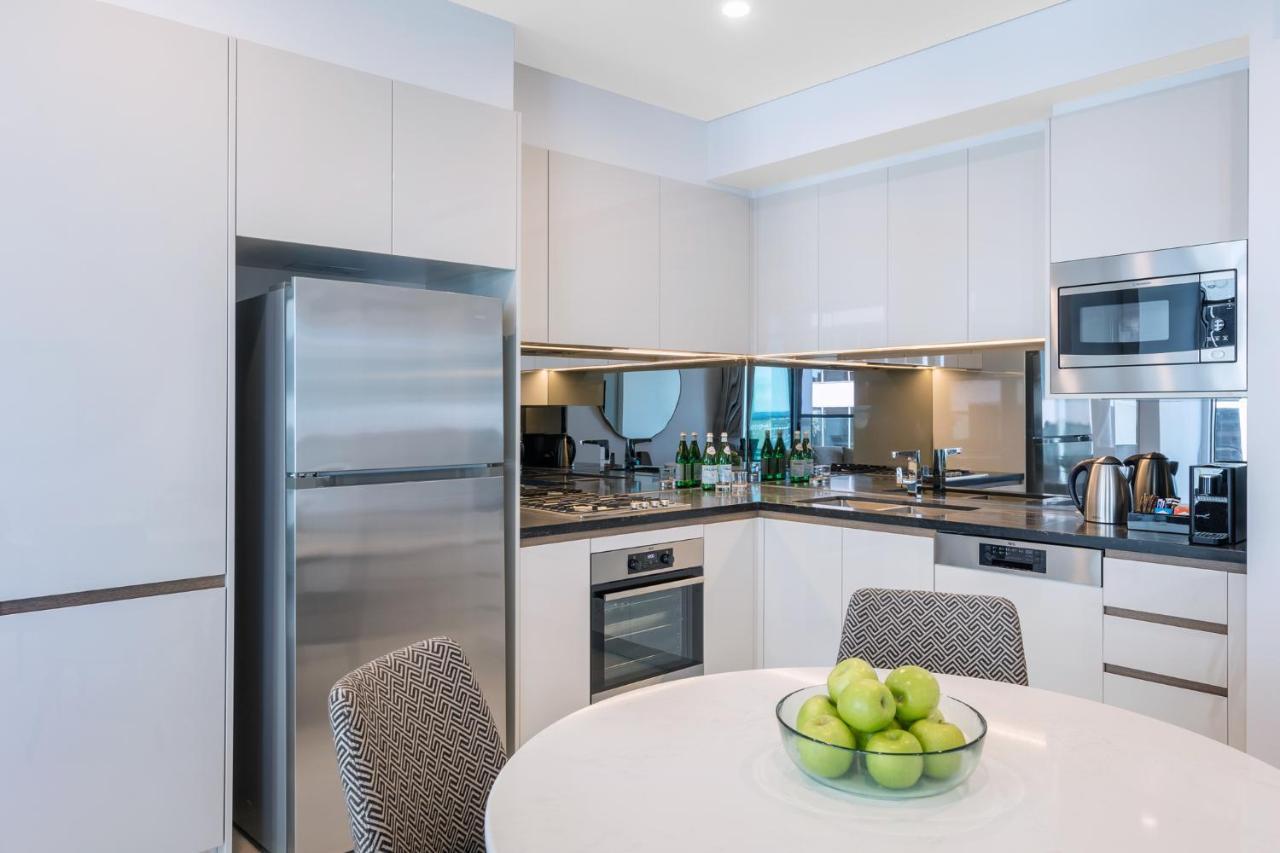 Meriton Suites Sussex Street, Sydney Zewnętrze zdjęcie The photo displays a modern kitchen with a sleek design. It features light-colored cabinetry and a countertop with a polished finish. On the left, there is a stainless steel refrigerator. The kitchen is equipped with various appliances, including an 