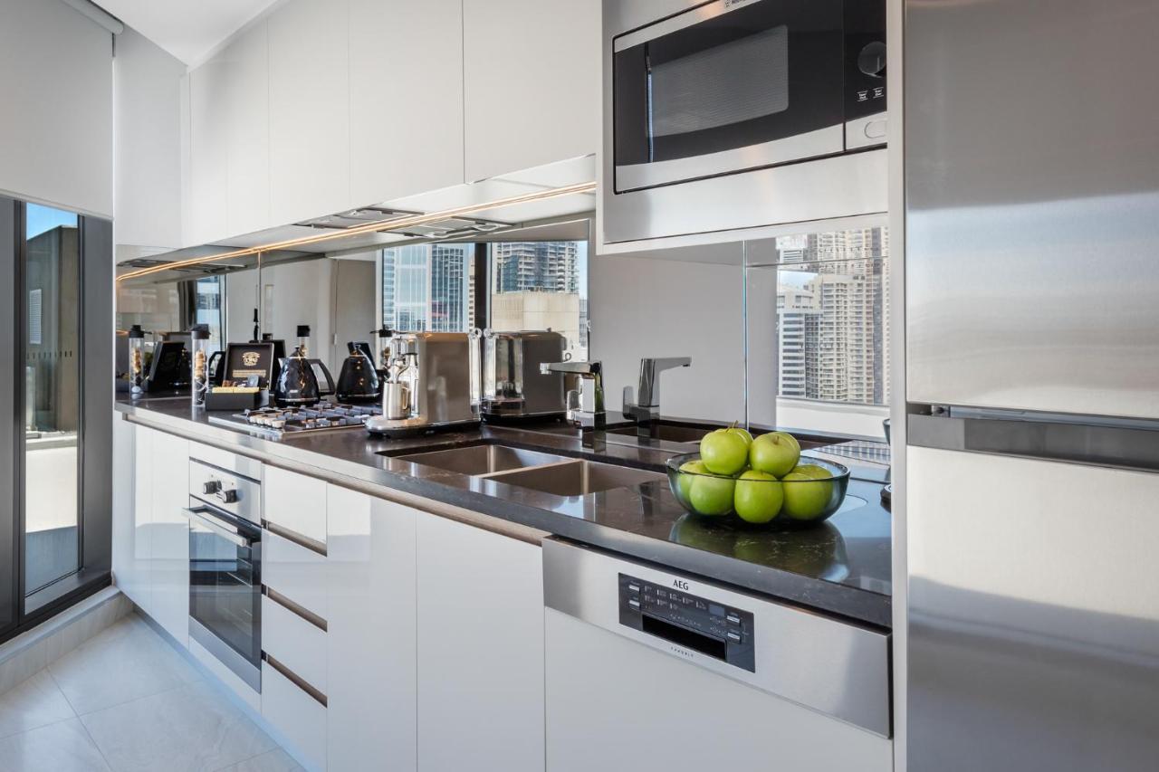 Meriton Suites Sussex Street, Sydney Zewnętrze zdjęcie The photo shows a modern kitchen featuring sleek cabinetry and stainless steel appliances. There is a glossy countertop with a bowl of green apples as a decoration. The kitchen includes a built-in oven, a microwave, and other kitchen gadgets, along w