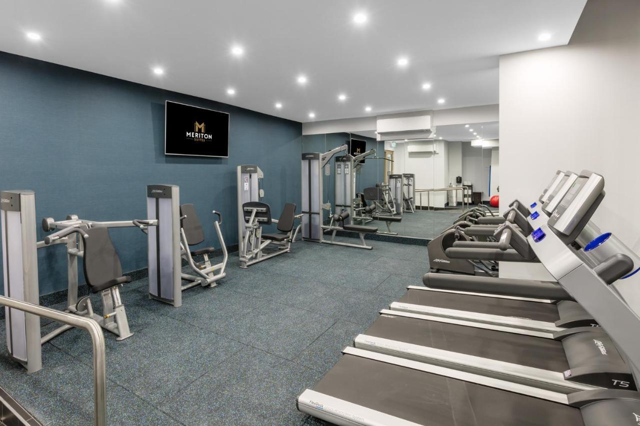 Meriton Suites Sussex Street, Sydney Zewnętrze zdjęcie The photo shows a modern gym interior. The space features several pieces of exercise equipment, including weight machines and stationary bikes. The walls are painted a calming color, and the flooring is carpeted. There are also mirrors on the walls, 