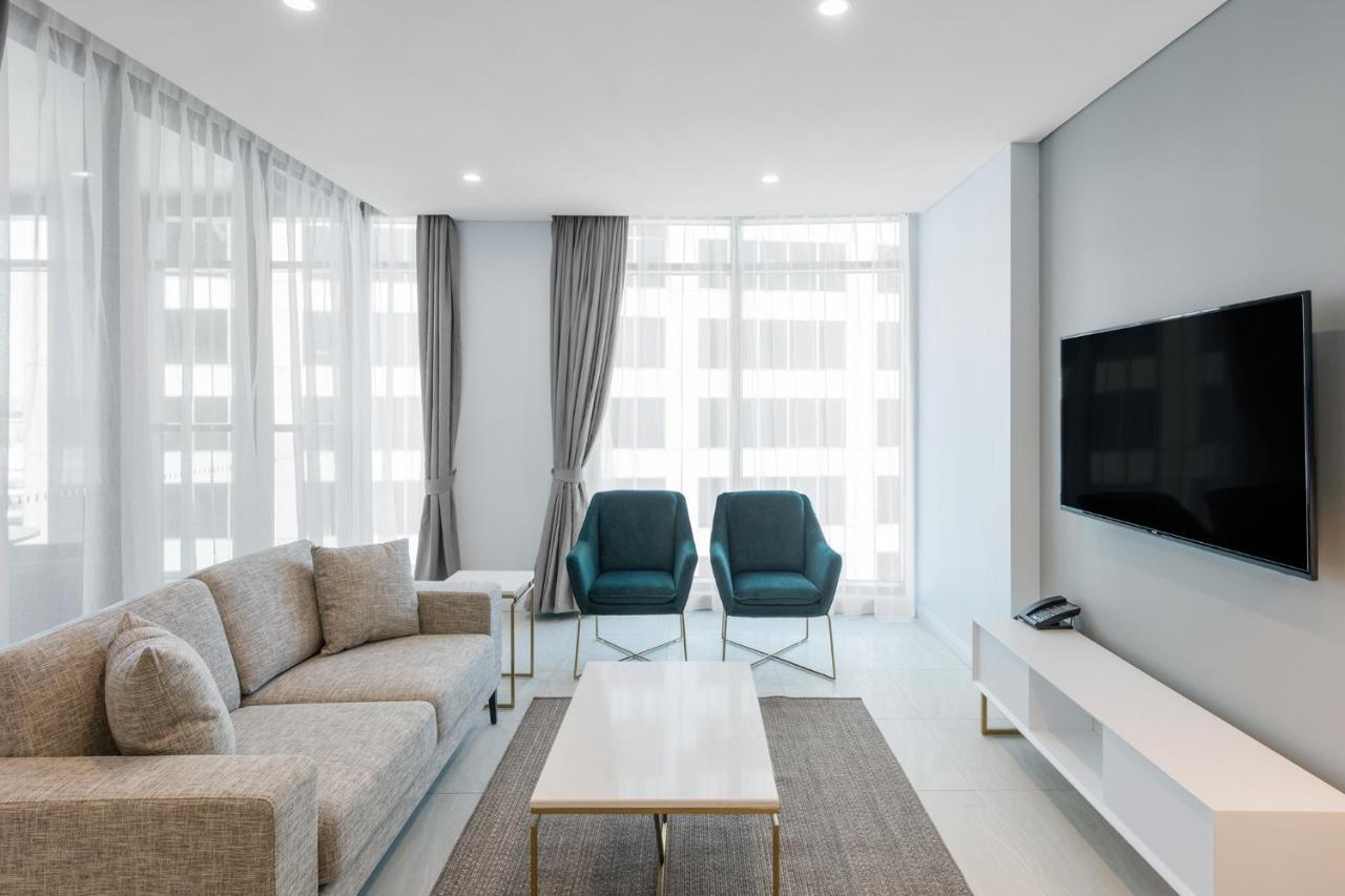 Meriton Suites Sussex Street, Sydney Zewnętrze zdjęcie The photo shows a modern living room equipped with a light gray sofa, two teal chairs, and a coffee table in the center. The room features large windows with sheer curtains, allowing natural light to illuminate the space. There is a white media conso