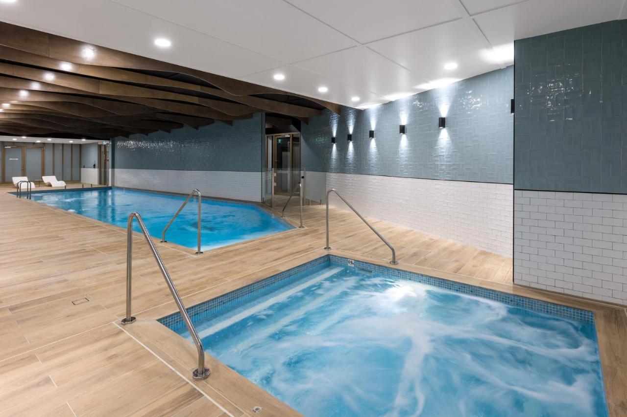 Meriton Suites Sussex Street, Sydney Zewnętrze zdjęcie The photo shows a modern indoor spa area. There are two pools: one is larger and has a clear blue water, while the other is smaller, possibly a hot tub, with jets creating bubbles. The walls are a mix of blue tiles and white tiles, and the floor is m