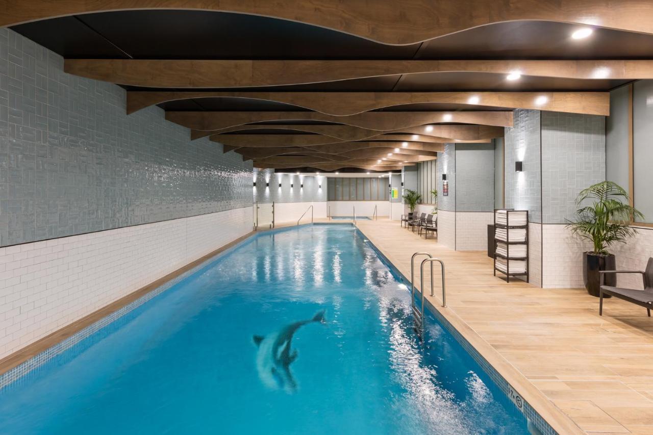 Meriton Suites Sussex Street, Sydney Zewnętrze zdjęcie The photo shows an indoor swimming pool. The pool features clear blue water, and there is a dolphin swimming in it. The surrounding area has a modern design with curved wooden beams on the ceiling, and the walls are tiled in light colors. There are a