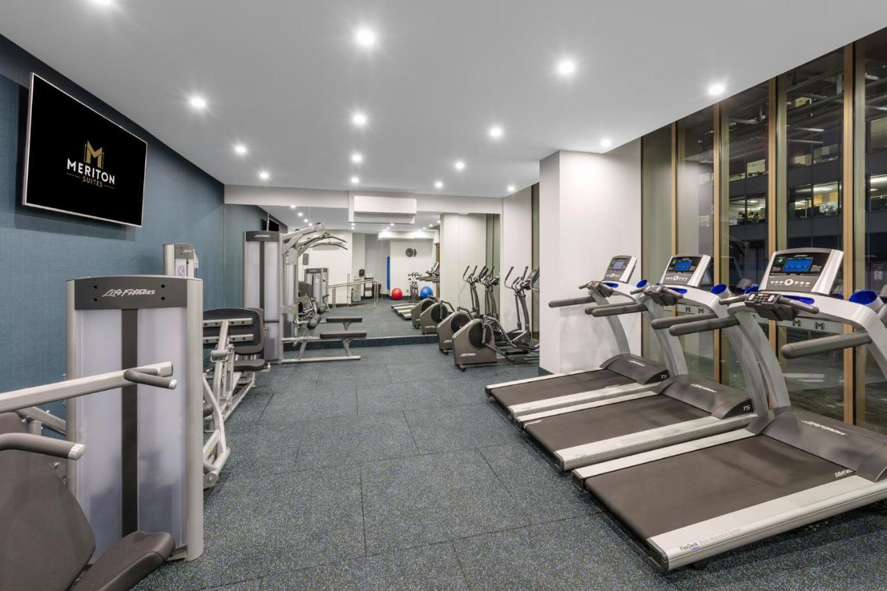 Meriton Suites Sussex Street, Sydney Zewnętrze zdjęcie The photo shows a modern gym space. It features various exercise equipment, including several treadmills and elliptical machines positioned along one side. On the other side, there are weight machines and additional fitness equipment. The gym has a c