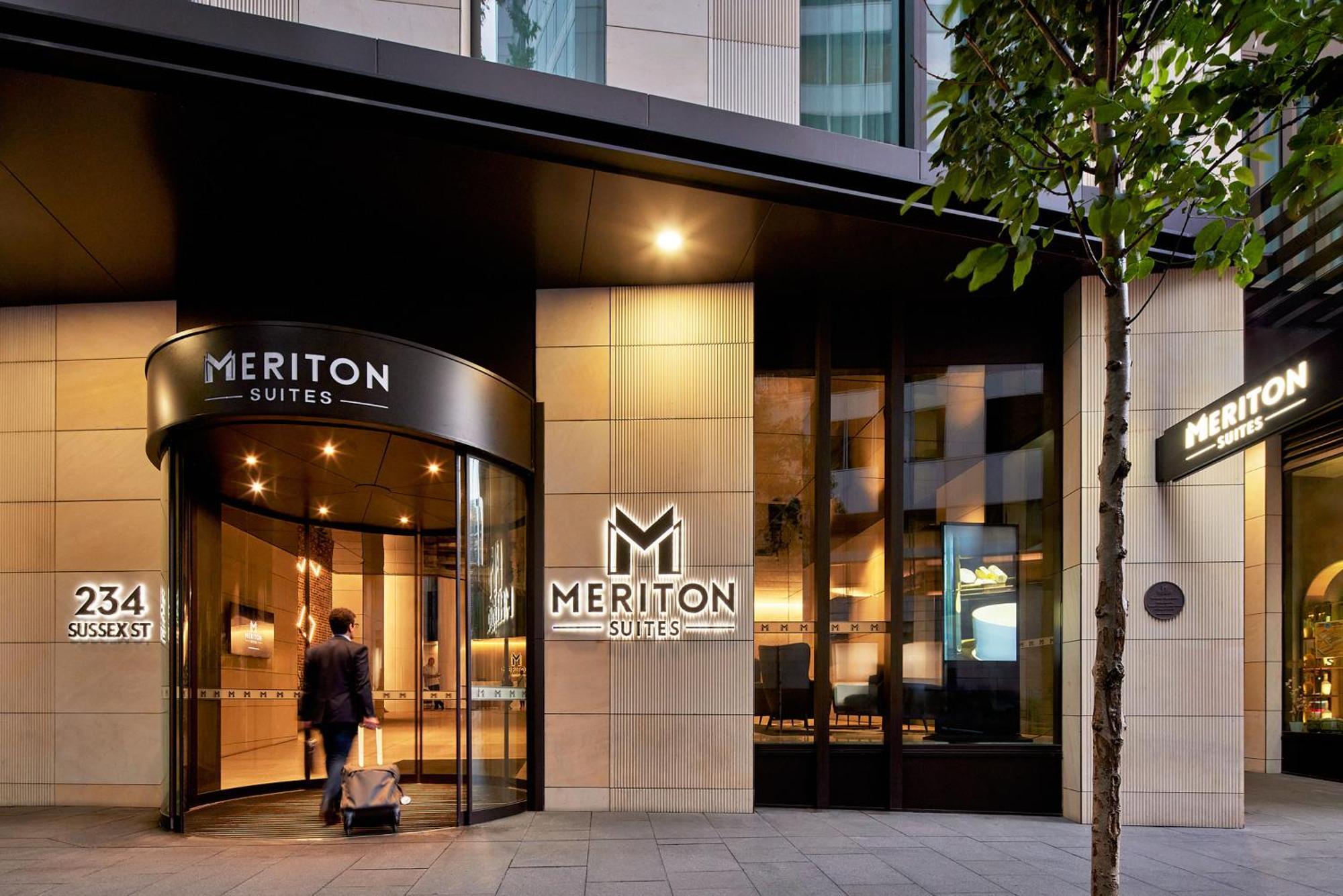 Meriton Suites Sussex Street, Sydney Zewnętrze zdjęcie The photo shows the entrance of a hotel or suite establishment named "Meriton Suites." The entrance features a revolving door and a large, illuminated sign with the name "MERITON SUITES." The facade is modern and sleek, with a combination of glass an