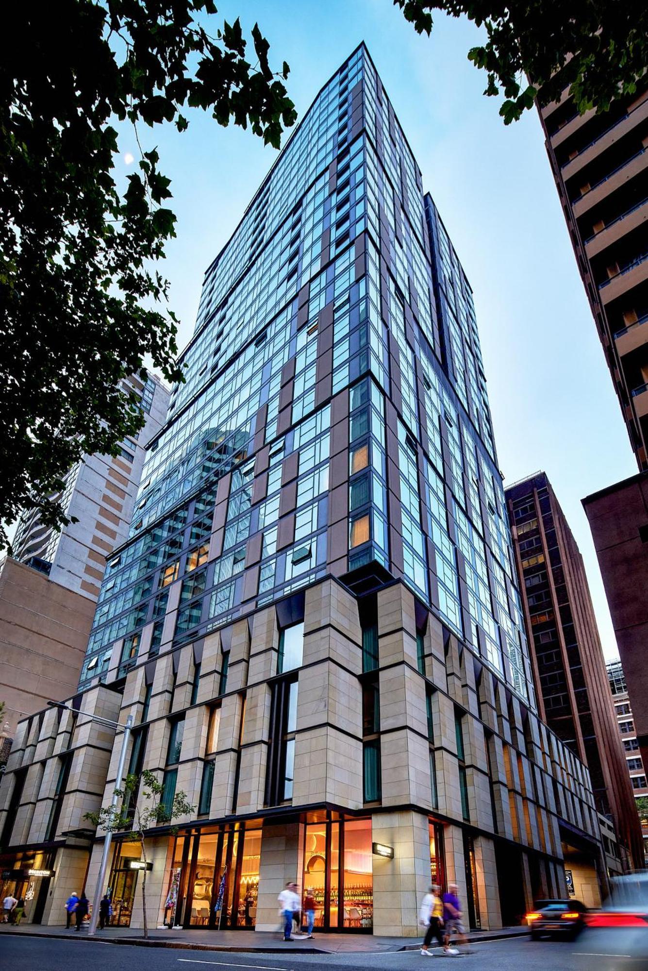 Meriton Suites Sussex Street, Sydney Zewnętrze zdjęcie The photo shows a modern high-rise building with a sleek, glass facade reflecting its surroundings. The structure features a combination of glass and concrete materials, with multiple stories visible. The lower part of the building has a sturdy, text