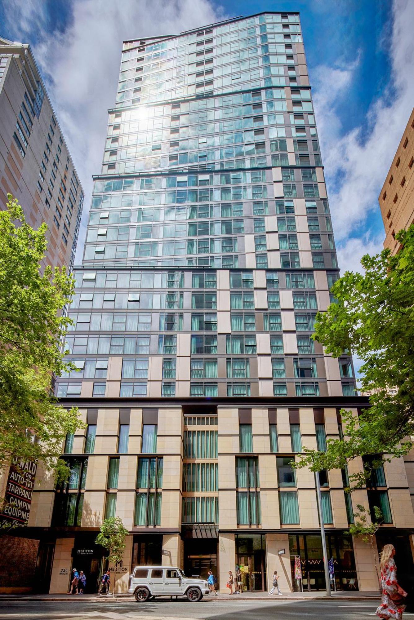 Meriton Suites Sussex Street, Sydney Zewnętrze zdjęcie The photo shows a tall modern building with a glass facade and various architectural design elements. The structure has multiple stories, with large windows that reflect the surrounding environment. At the base, there are sections that appear to have