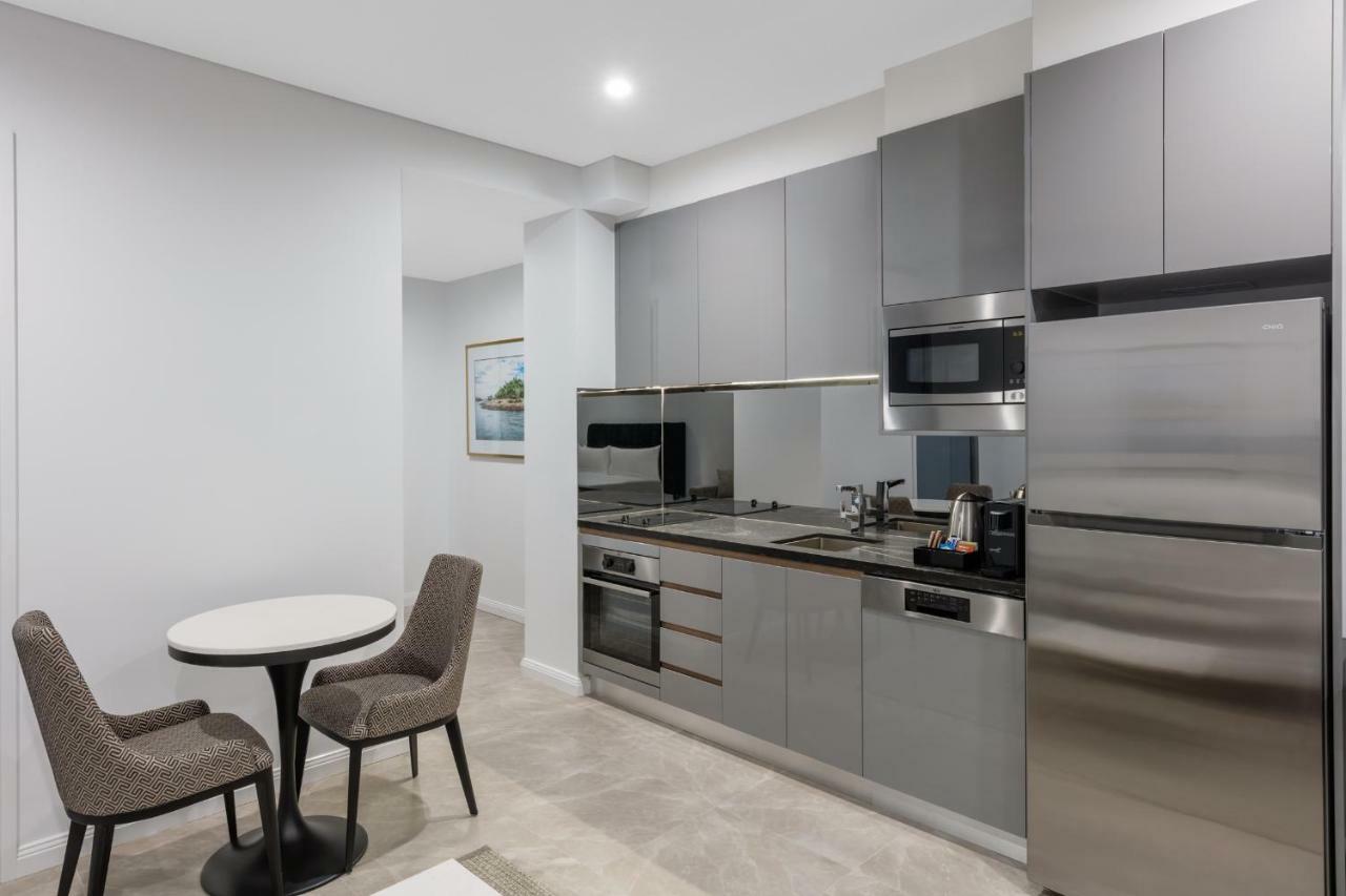 Meriton Suites Sussex Street, Sydney Zewnętrze zdjęcie The photo shows a modern kitchen area that features a sleek design. The cabinetry and appliances are in shades of gray, giving it a contemporary look. There is a stainless steel refrigerator, microwave, and oven, along with a sink and cooking area. 
